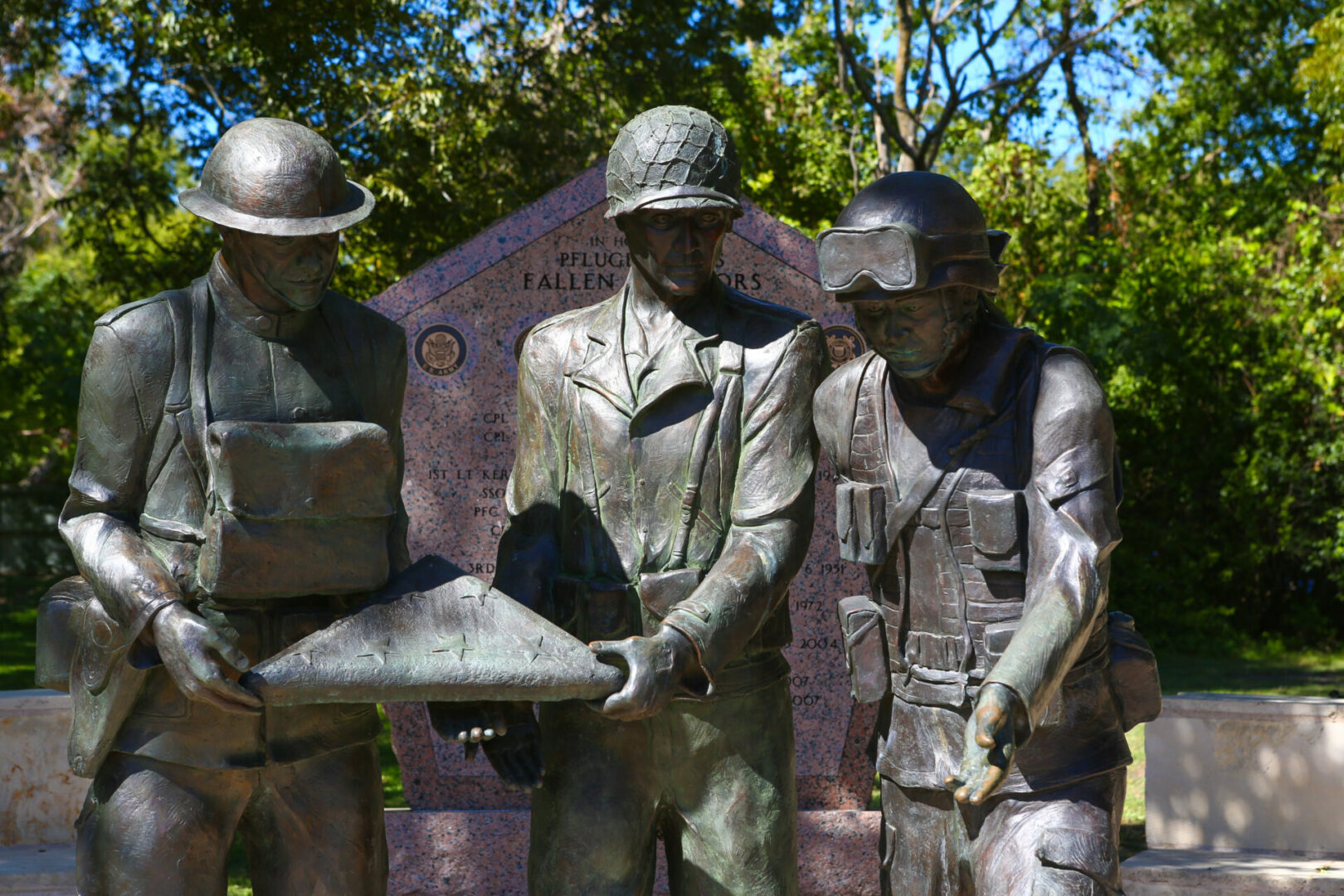three bronze statues of men in uniforms are holding a box