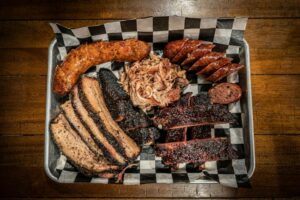 a tray filled with meats and sausages on top of a wooden table